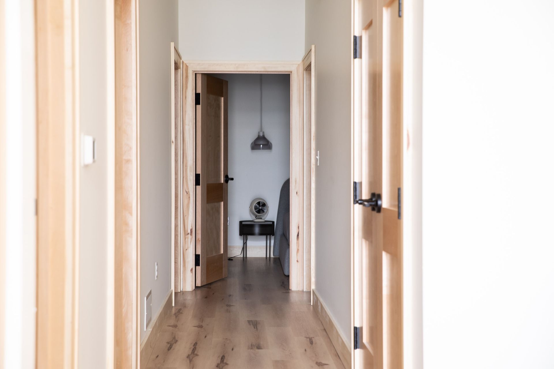 A hallway with wooden floors and doors leading to a bedroom.