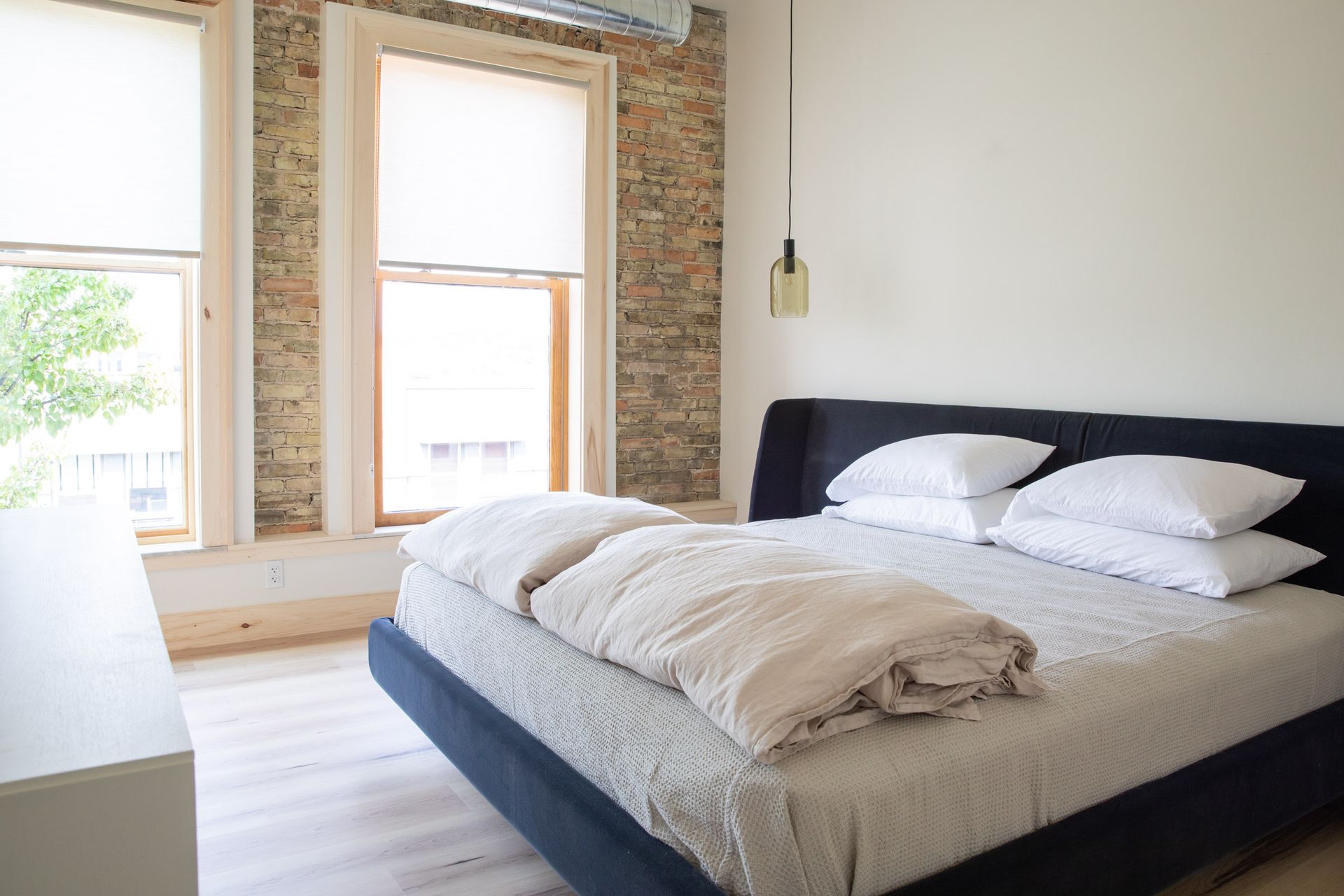 A bedroom with a bed , two windows and a brick wall.
