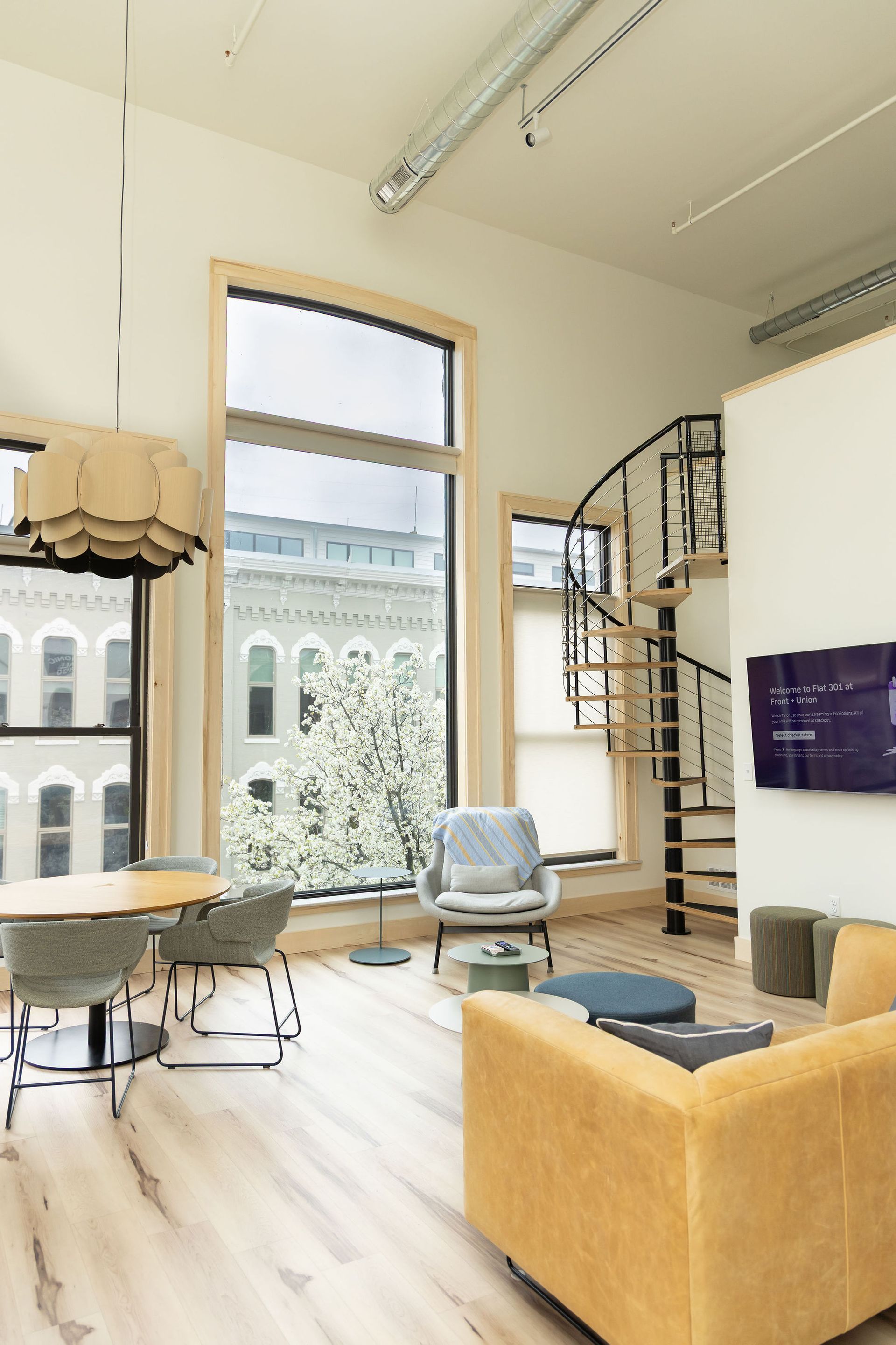 A living room with a yellow couch , chairs , a table and a spiral staircase.