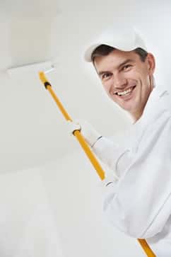 Painter with roller painting wall white and smiling