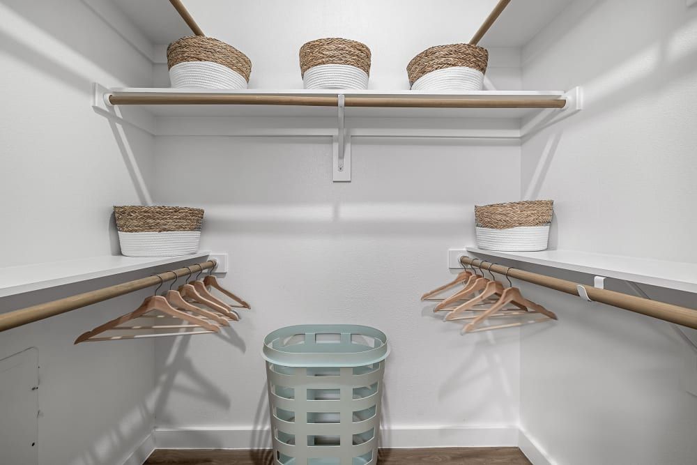 A tidy and minimalistic walk-in closet featuring white walls and wooden shelves. There are three woven baskets on the top shelf, a few wooden hangers on the lower closet rod, and an empty light blue laundry basket on the floor to the left. The closet is well-organized and gives a sense of calm and order at 44 South in Austin, TX.