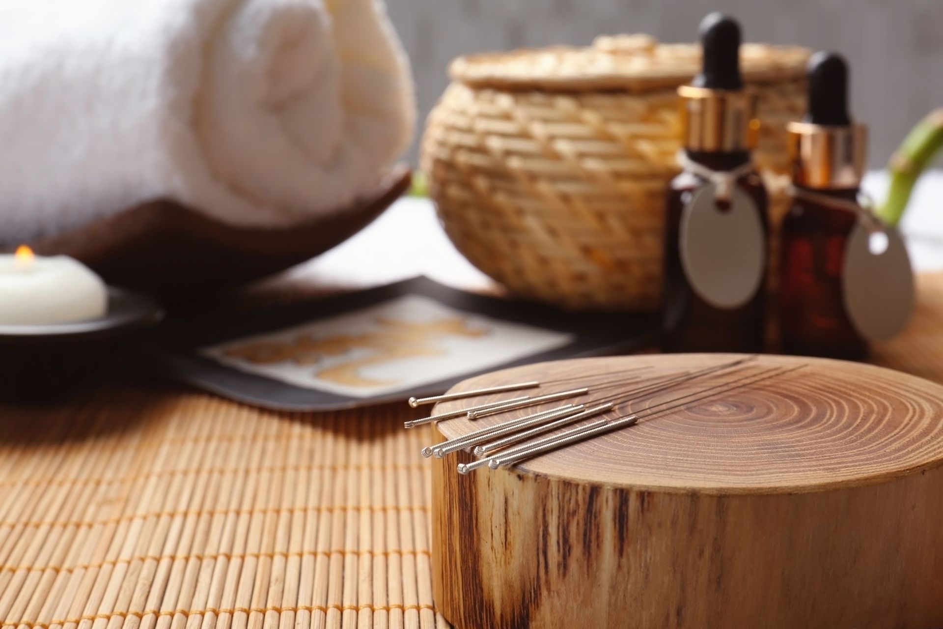 Acupuncture needles are sitting on a wooden block on a bamboo mat.