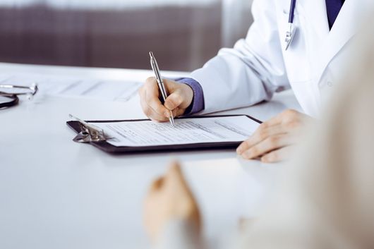 A doctor is writing on a clipboard with a pen.