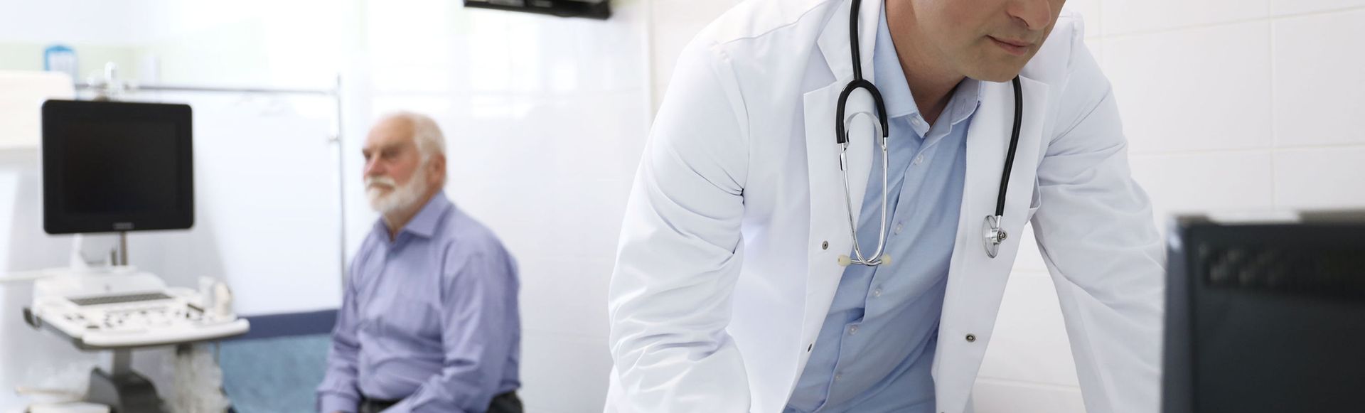 A doctor is standing in front of a computer while a patient sits in a chair.