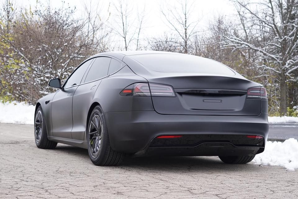 Black matte Tesla sedan parked on a snow-covered roadside.