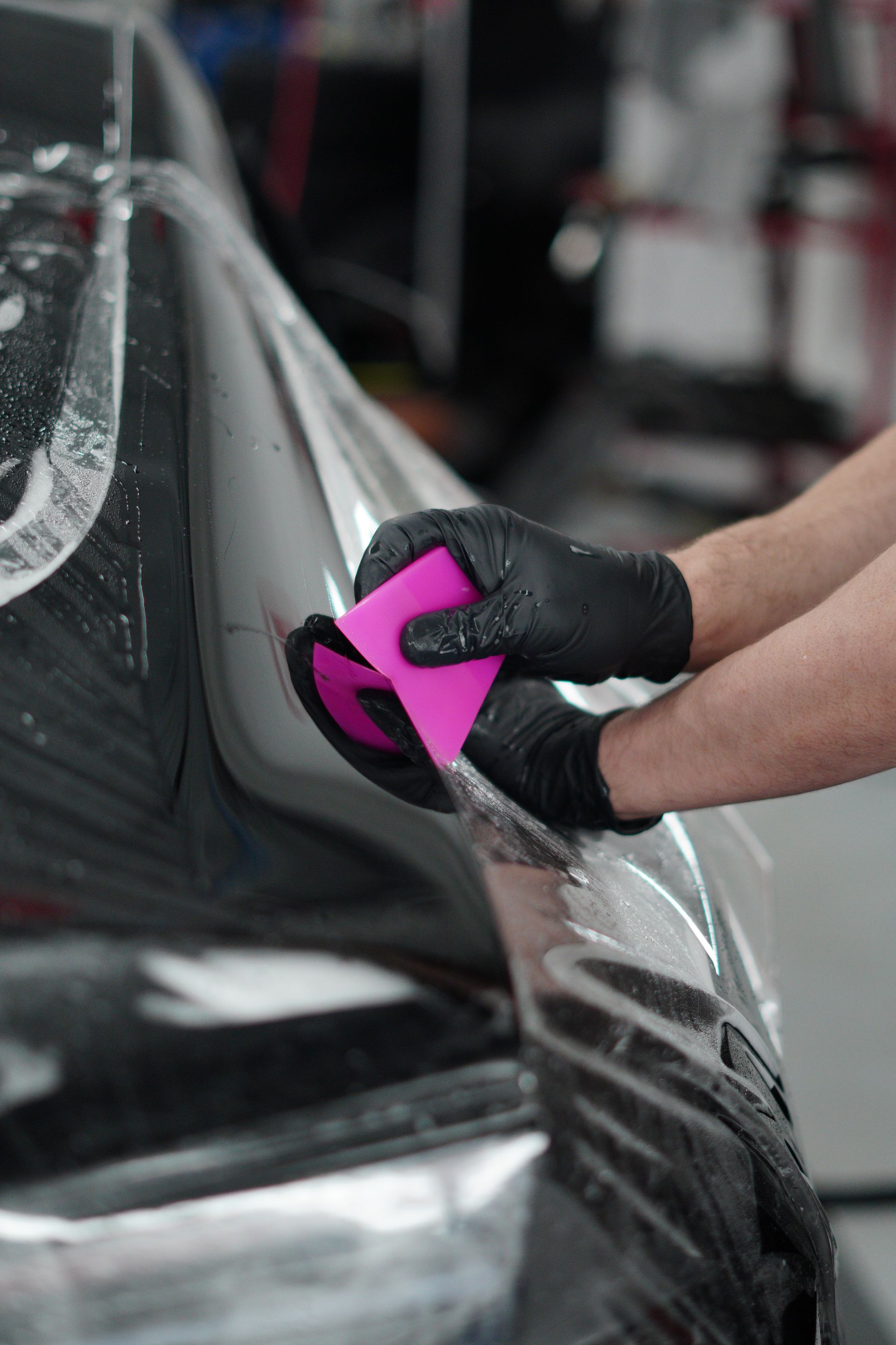 A person is cleaning a car with a pink sponge.