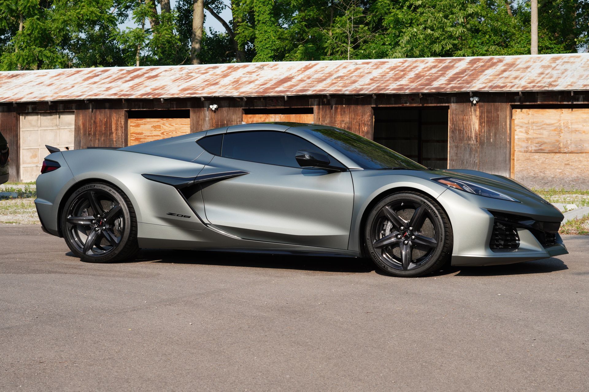 A silver sports car is parked in front of a barn.