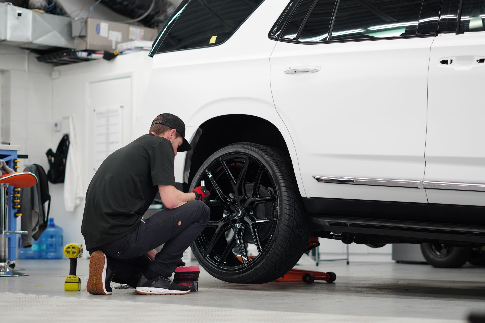 A man is kneeling down next to a white suv in a garage.