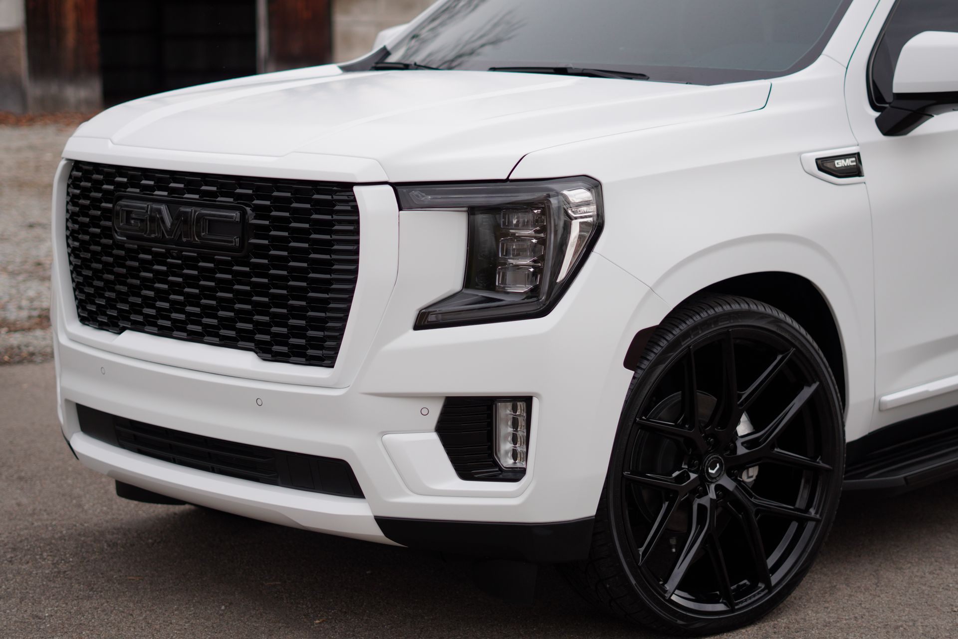 A white gmc sierra with black wheels is parked on the side of the road.