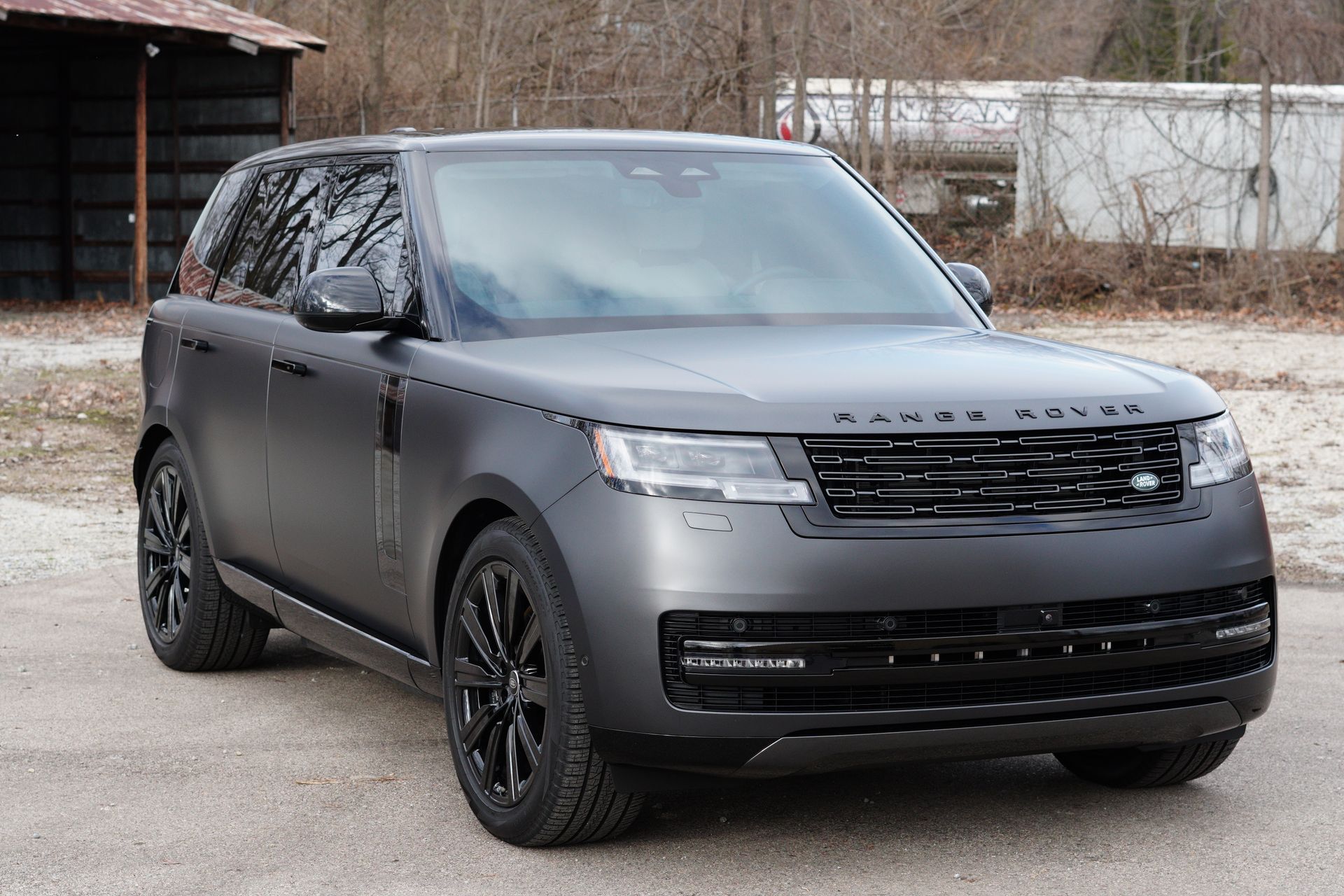 Gray Range Rover SUV parked on a gravel lot; black wheels, matte finish.