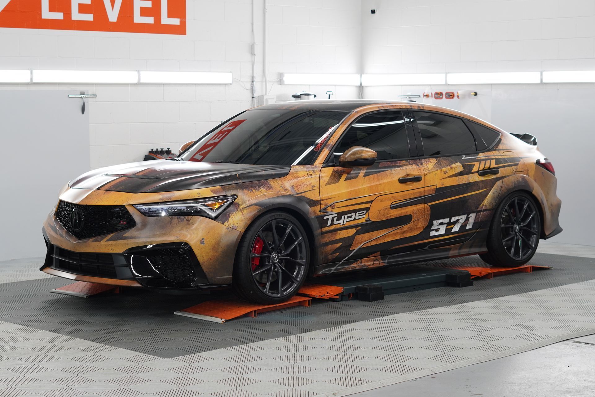 Custom-wrapped Acura Integra in garage. Orange, black wrap; black wheels, red brake calipers; on orange mats.