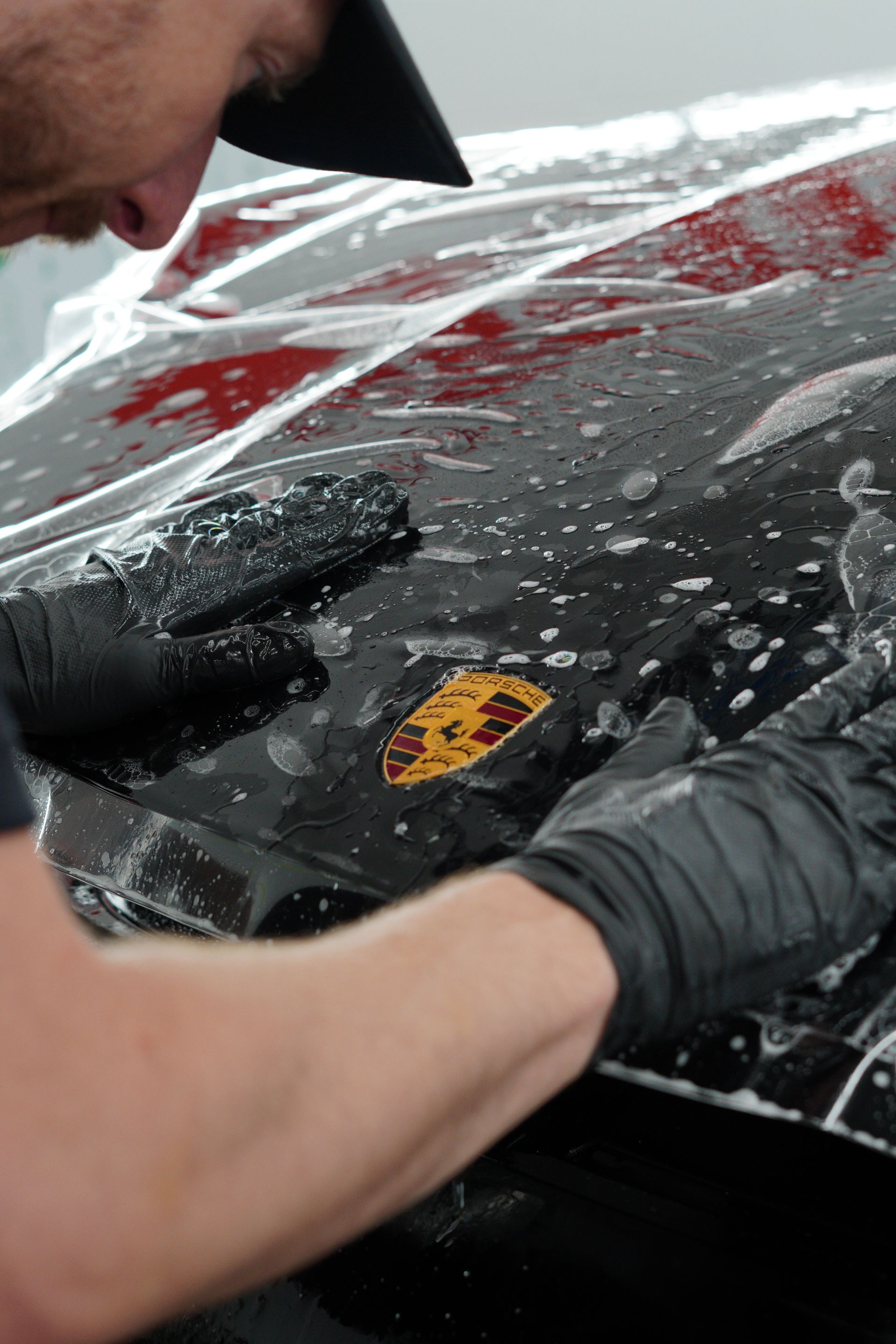 A man is covering the hood of a car with plastic wrap.