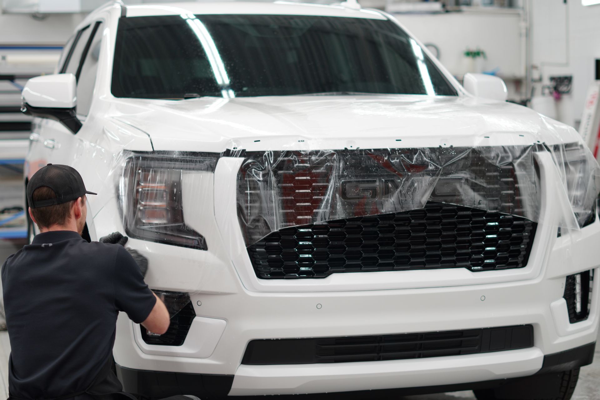 A man is applying a protective film to the front of a white suv.