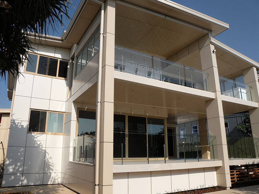 Modern Two-story Building With White Siding, Glass Balconies, And Large Windows. Sunny Day Setting