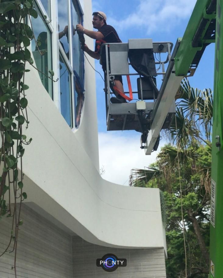 A Man Is Cleaning A Window With A Squeegee — Scratchless Glass Australia in Maroochydore, QLD