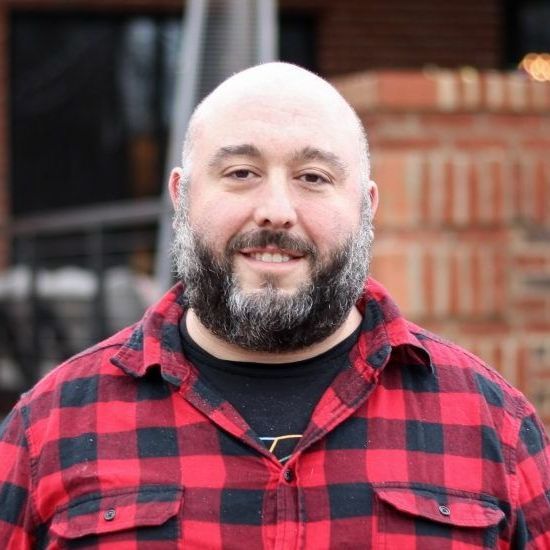 A bald man with a beard wearing a red and black plaid shirt