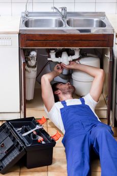 A man is laying on the floor fixing a sink.