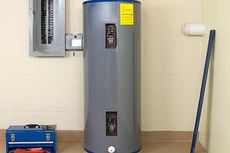 A water heater is sitting in a room next to a toolbox and a mop.