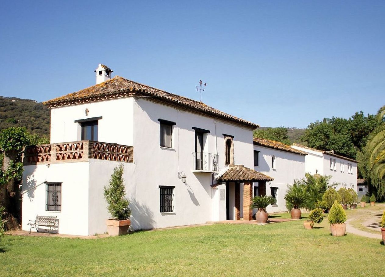 Wit stucwerkhuis met een bruin pannendak, groen gazon en bomen op een zonnige dag.