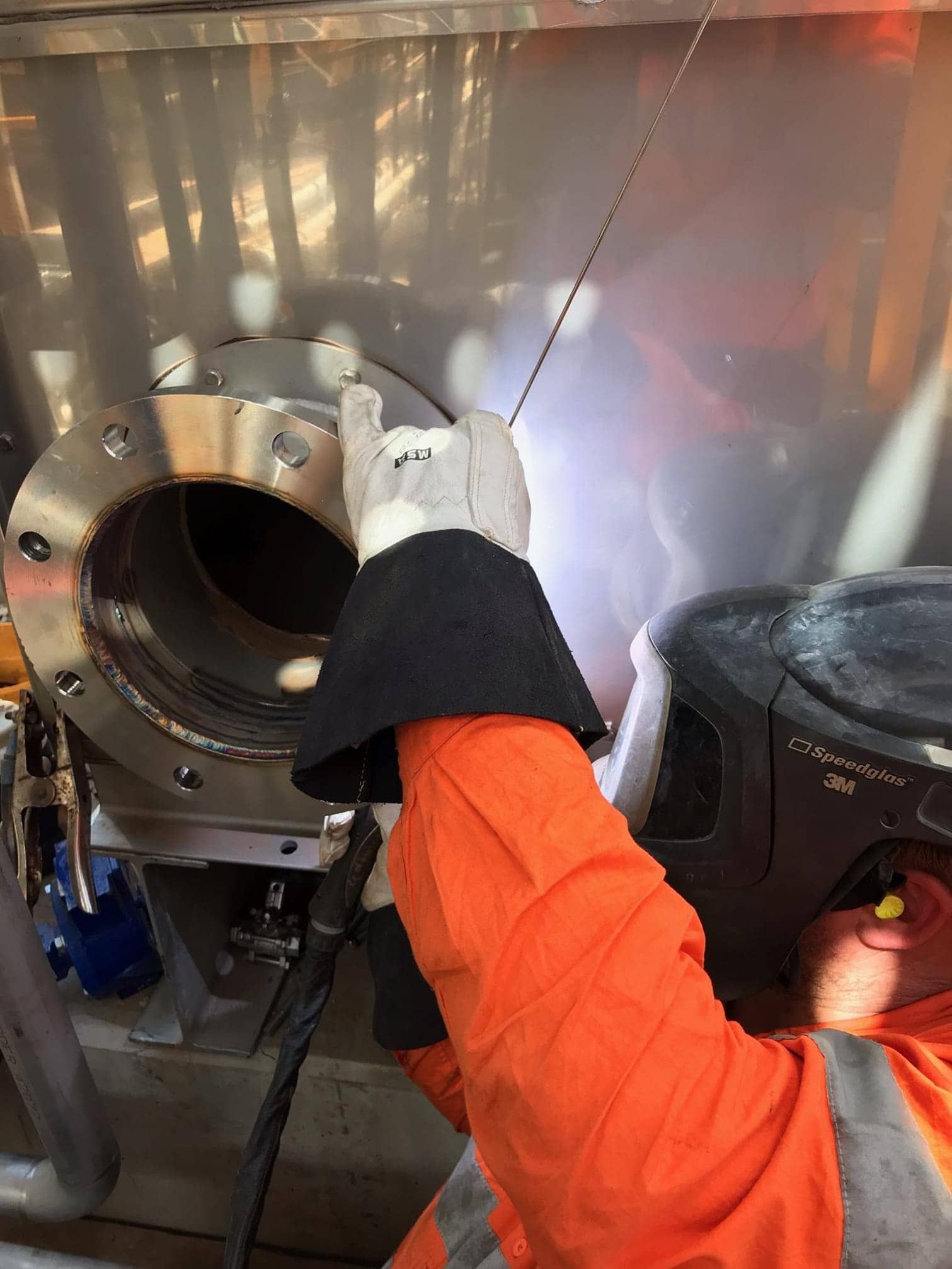 A Man In An Orange Jacket Is Welding A Metal Pipe — Bigdog Welding and Fabrication Pty Ltd In Currajong, QLD