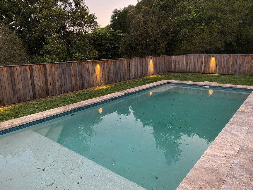 A Large Swimming Pool With a Wooden Fence Around It — Brightway Electrical in Ballina, NSW