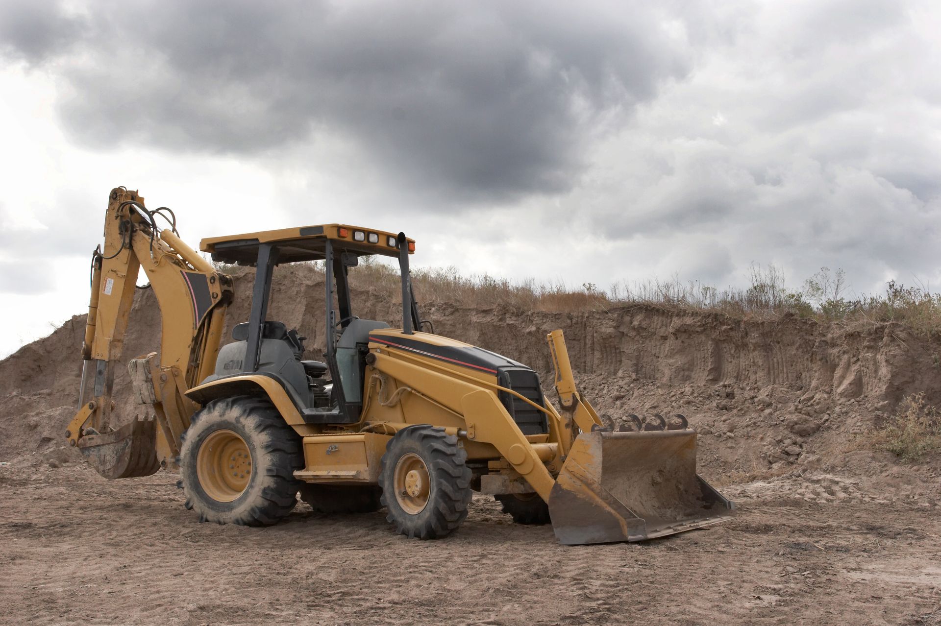 Yellow excavator dumping dirt outdoors in bright sunlight.