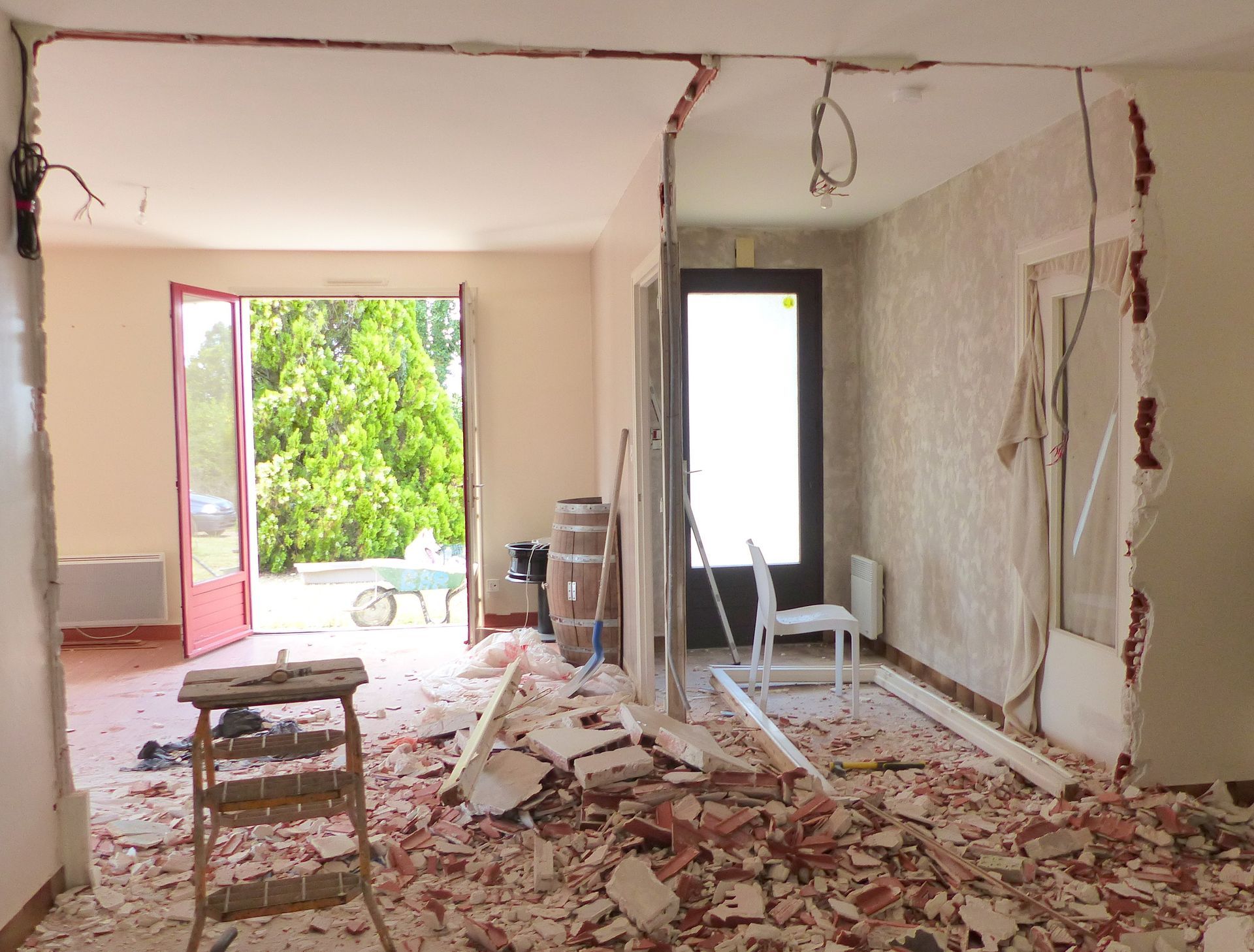 Orange excavator demolishing interior of a warehouse, rubble on the floor, blue dumpster.