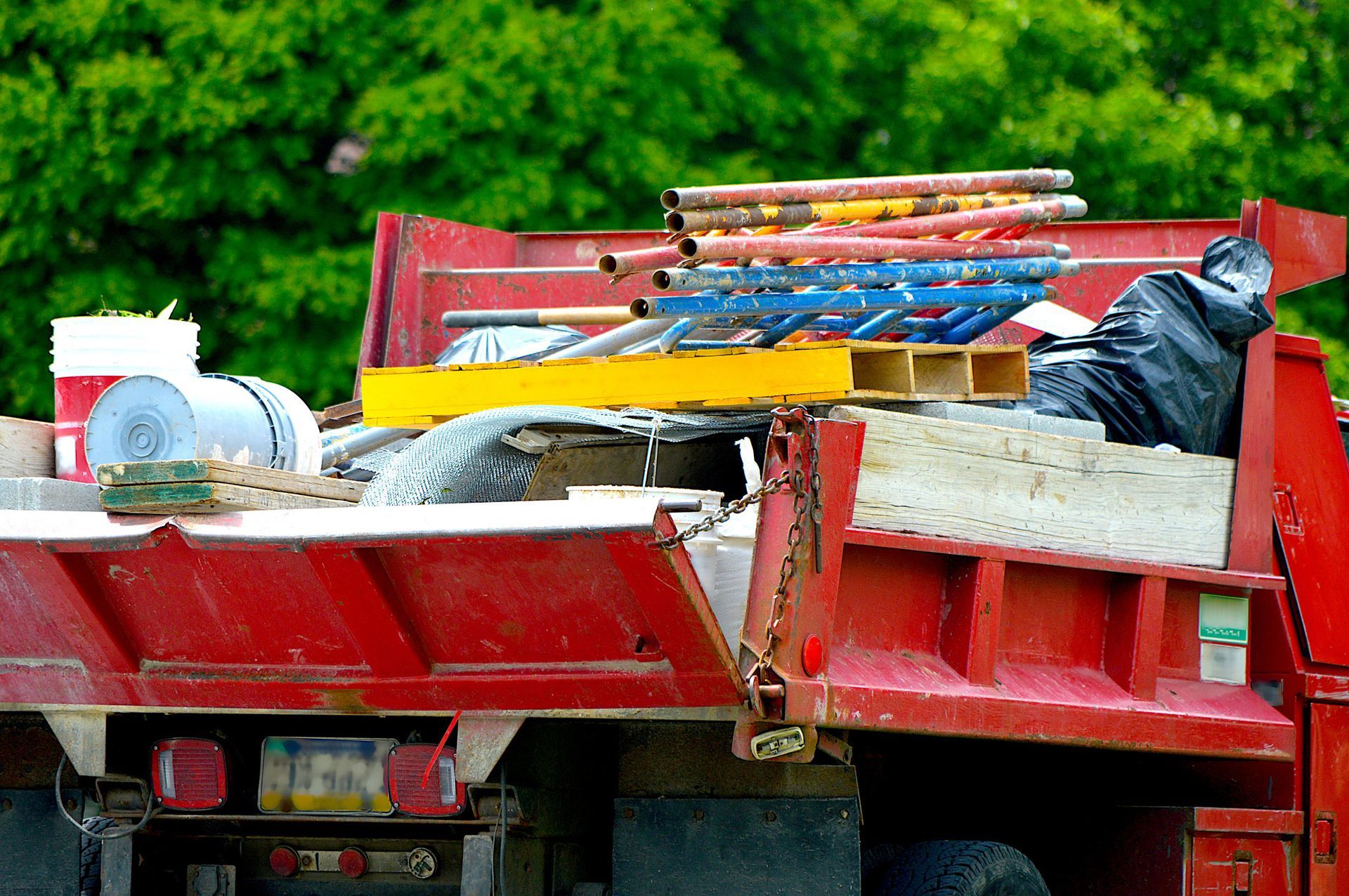 Red dump truck bed filled with construction debris, with a green tree background.