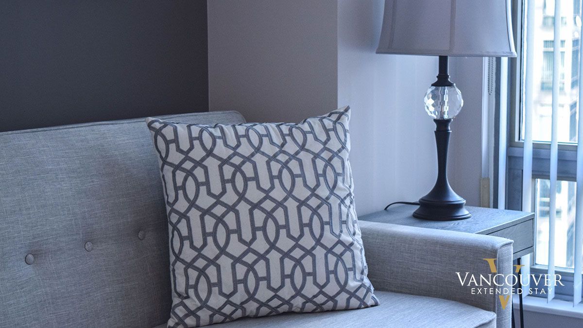 Sofa pillow with a line design on top of a sofa chair next to a lamp 