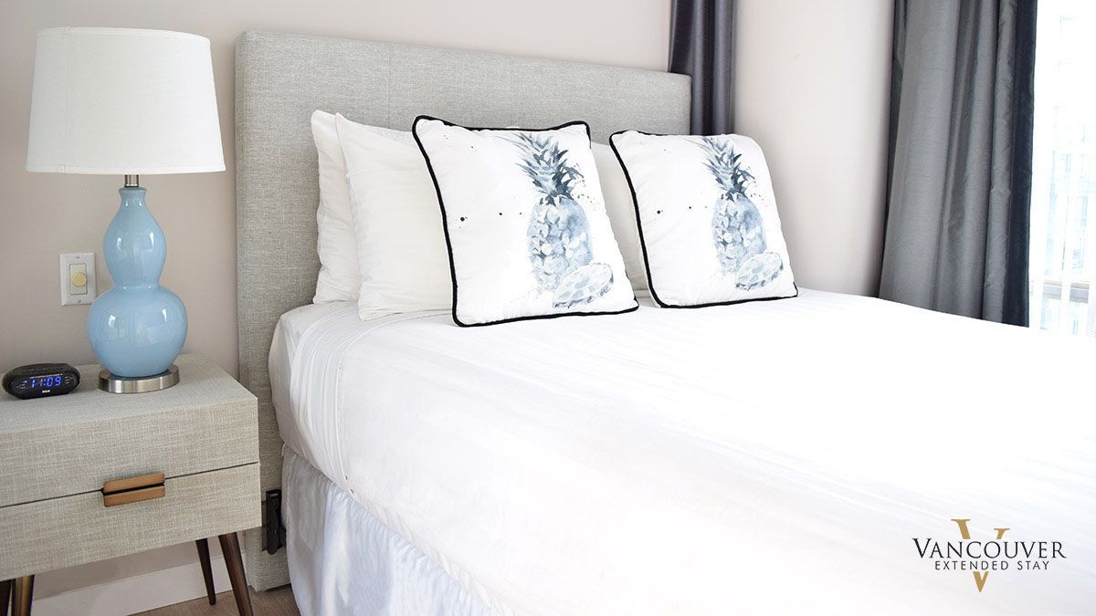 Two white pillows with a blue pineapple design on a twin size bed next to a baby blue lamp