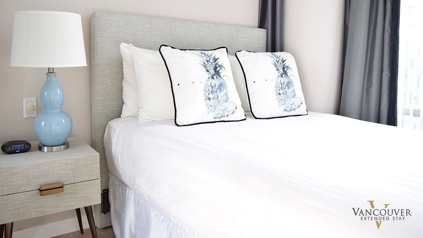 Two white pillows with a blue pineapple design on a twin size bed next to a baby blue lamp