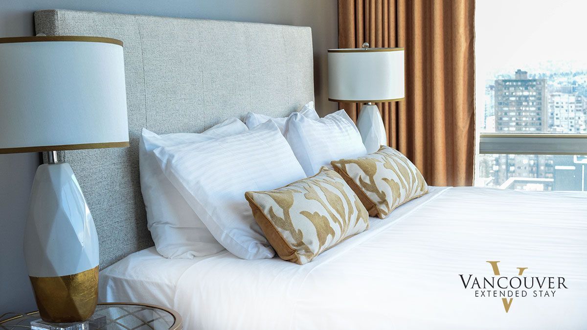 Two small yellow pillows, two medium size white pillows, and two large white pillows on a queen size bed next to a white lamp