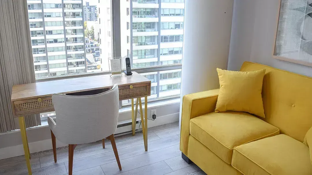 yellow sofa next to a window, wooden desk, and a wooden chair