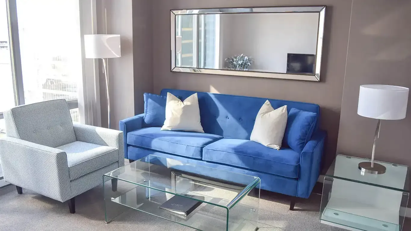 Two plain white sofa pillows on a blue sofa next to a mirror and a glass coffee table