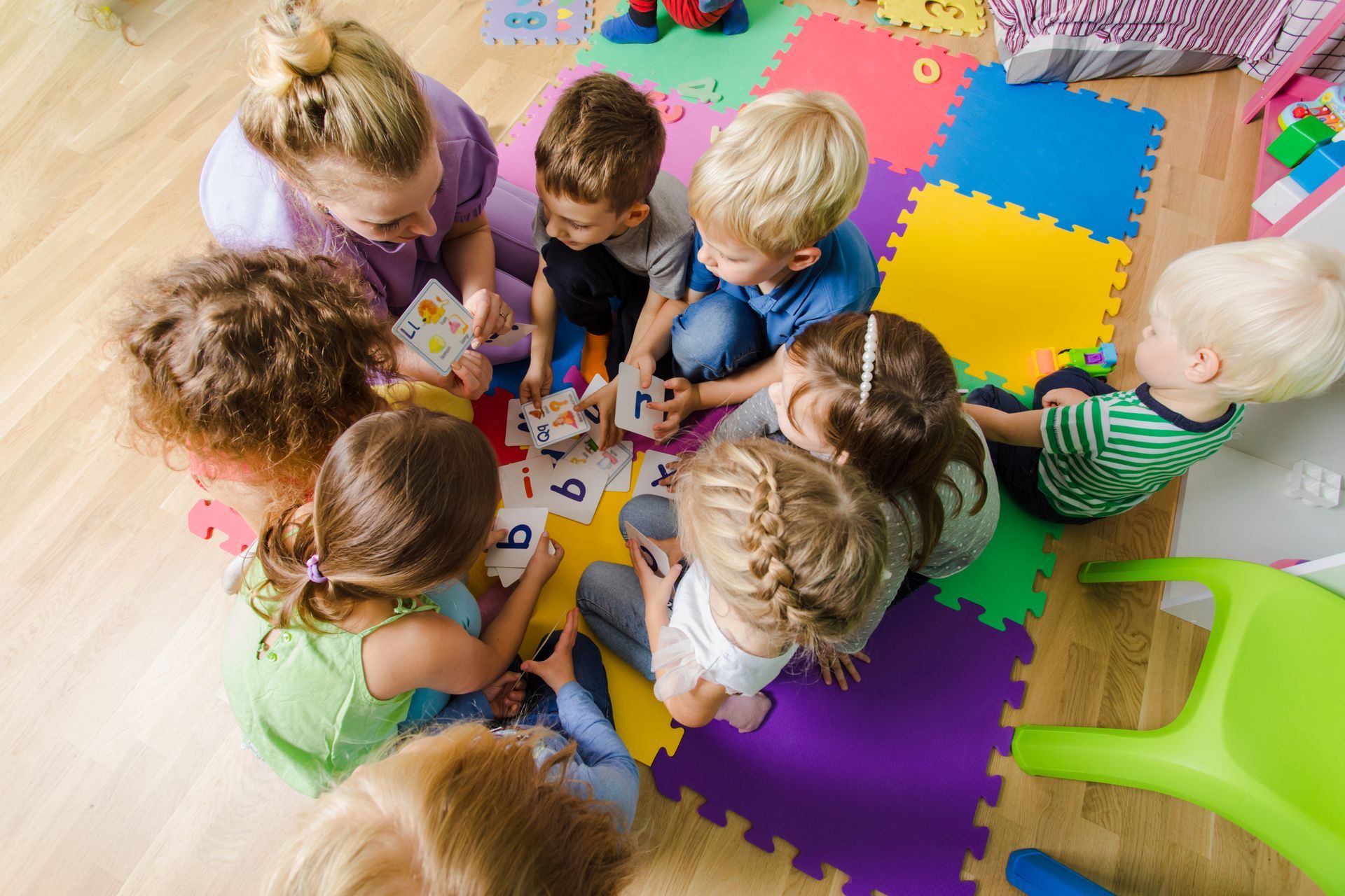 Children sitting on colorful foam mats learning letters together during a group activity in class