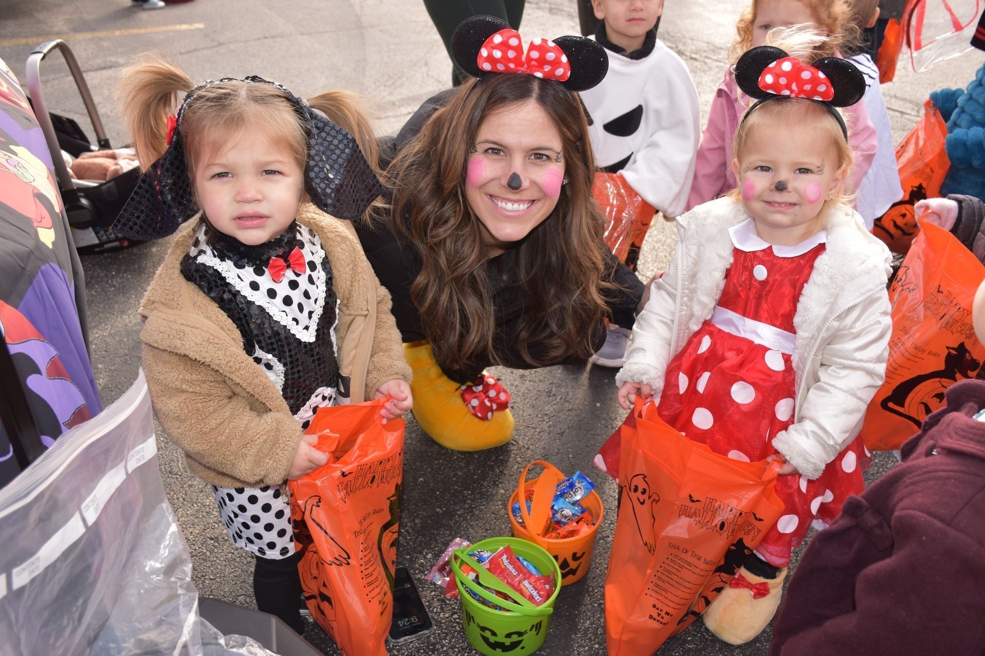Woman and two children in Minnie Mouse costumes, smiling, holding treat bags.