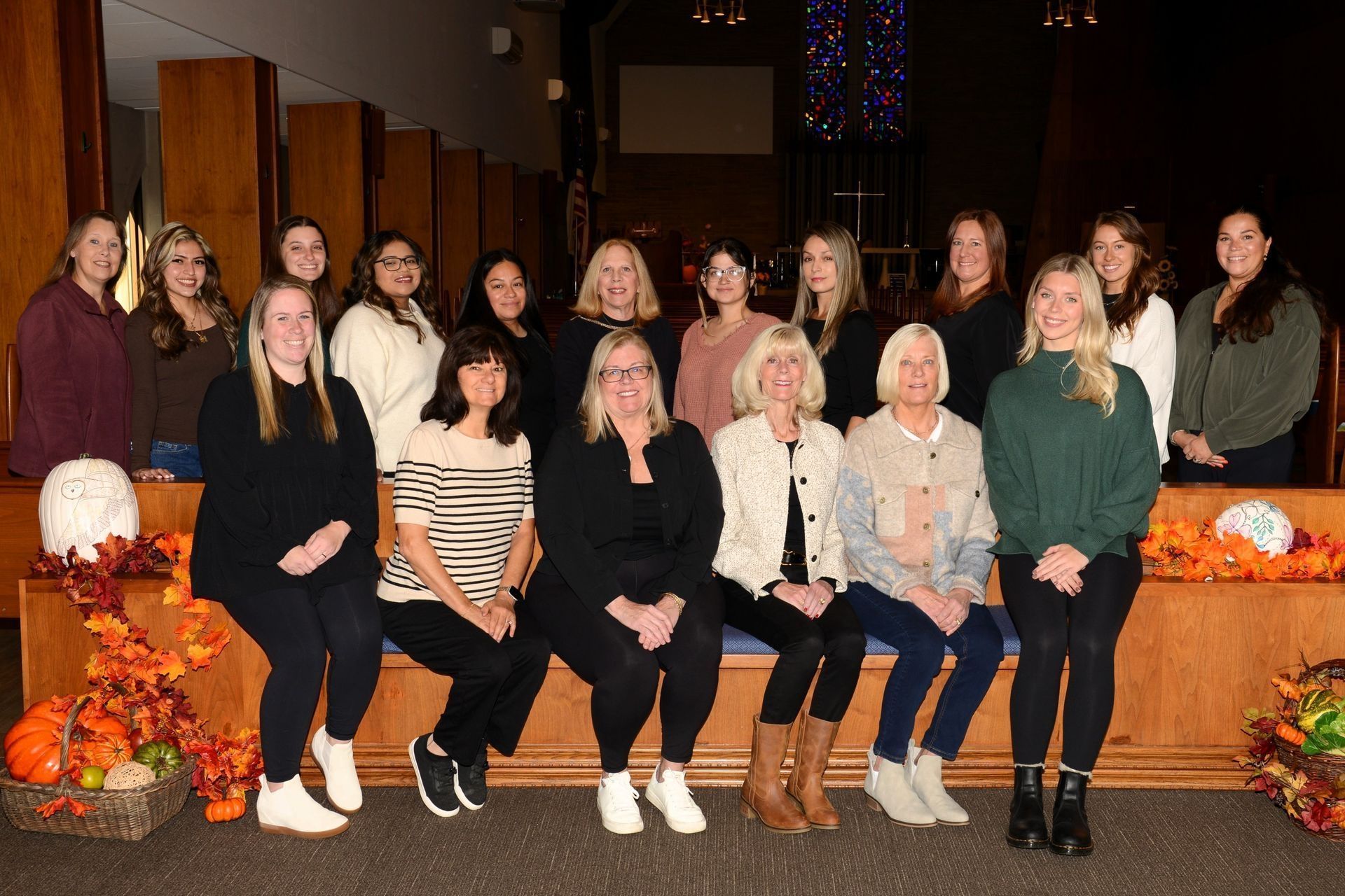 Group of women posing together, seated and standing near fall decor.