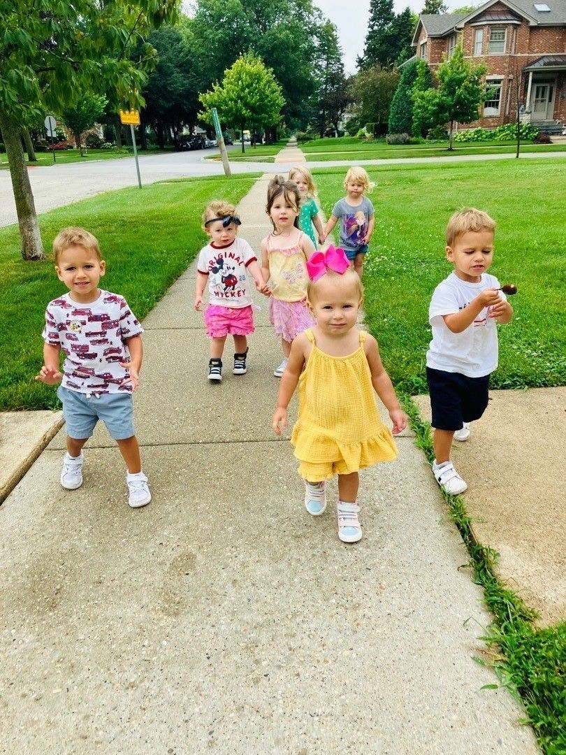 Group of children walking on a sidewalk outdoors; sunny day.