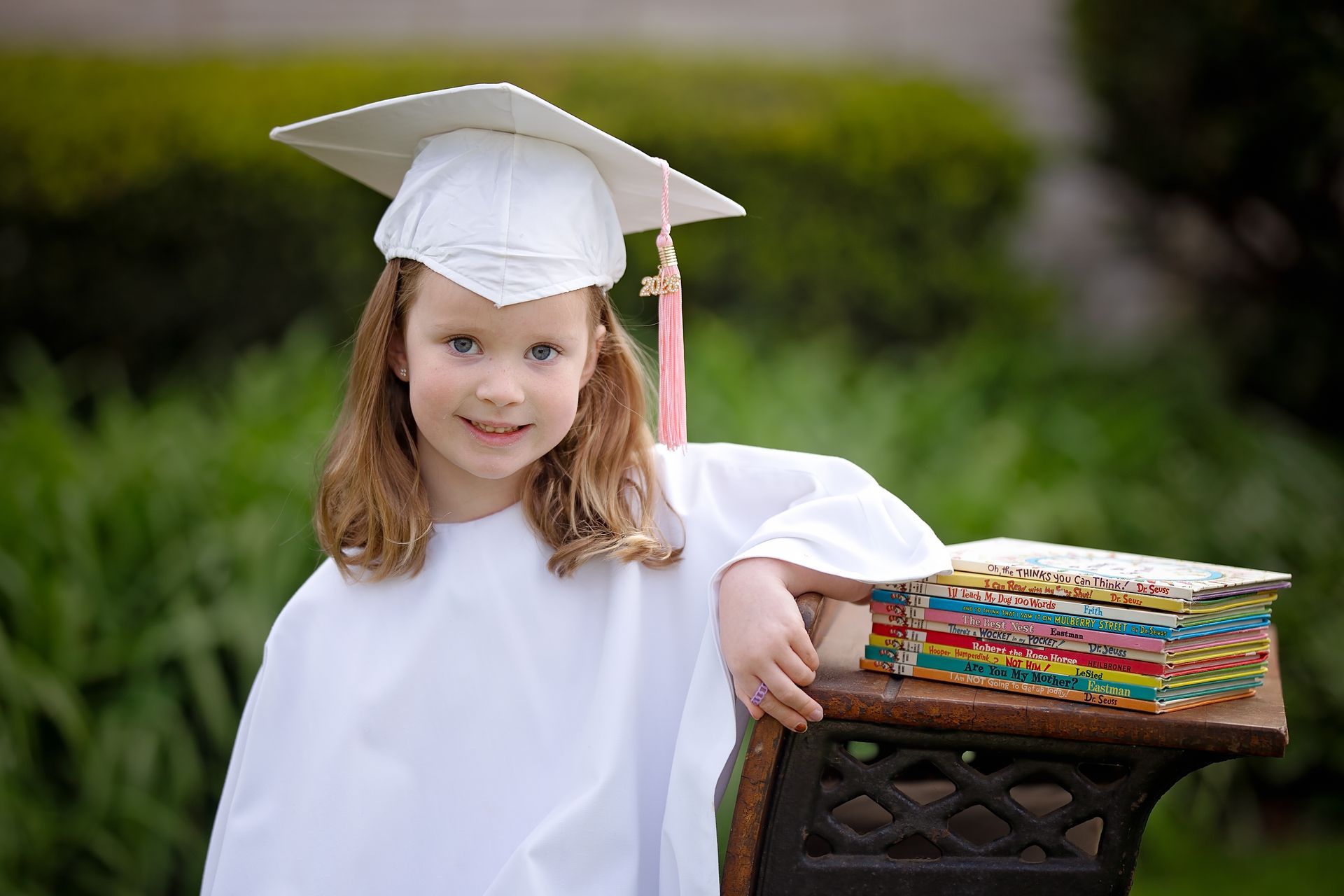 Girl in white graduation cap and gown smiles against a gray background.