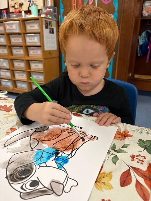 Child in koala hat, blue sequin jacket, and orange bow tie waves while holding a microphone on stage.