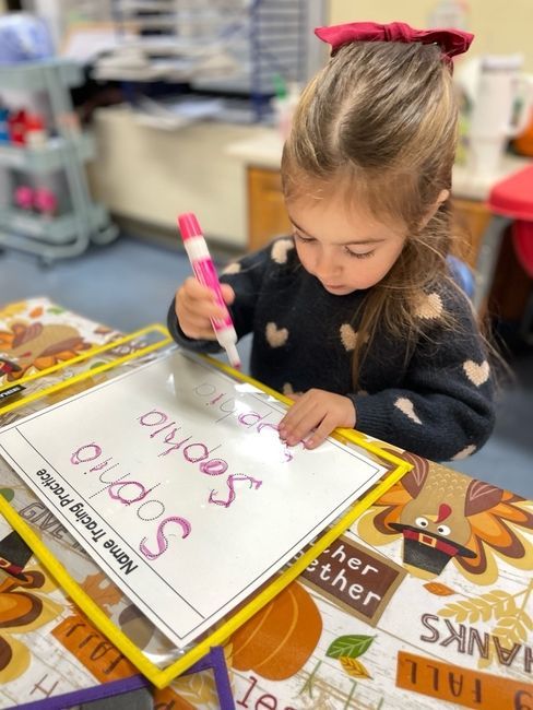 Child on playground, wearing a patterned hat and silver jacket, smiling at the camera.