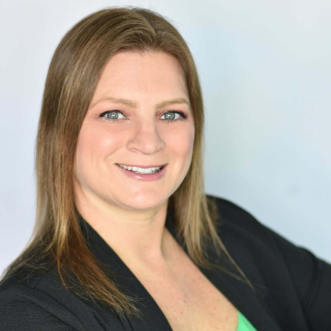 A woman wearing a black jacket and a green shirt smiles for the camera