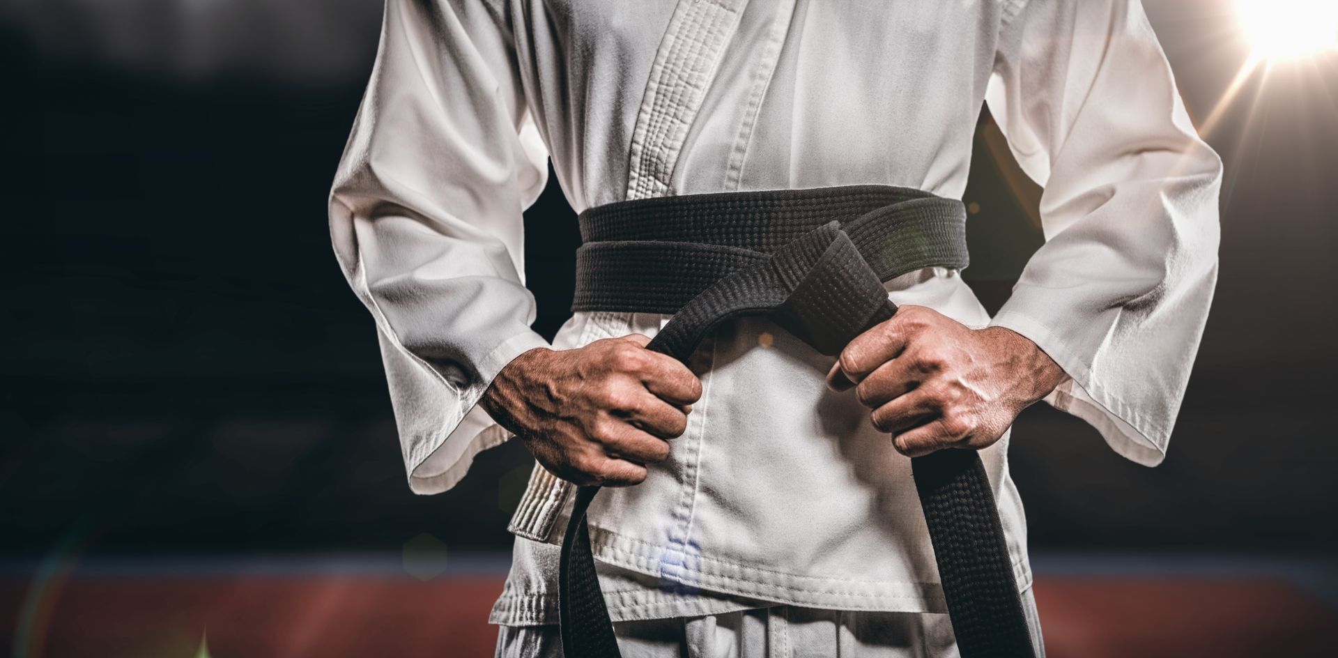 A man in a karate uniform is tying his black belt.