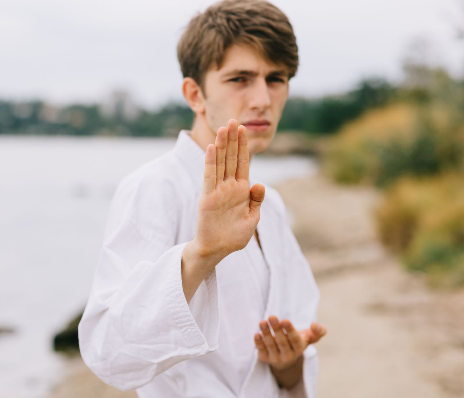 A young man in a white karate uniform is making a stop sign with his hand.