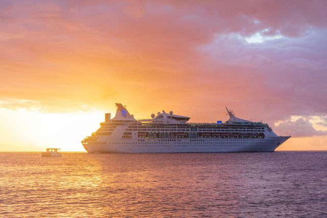 Cruise ship sailing on calm water at sunset with a colorful pink-orange sky