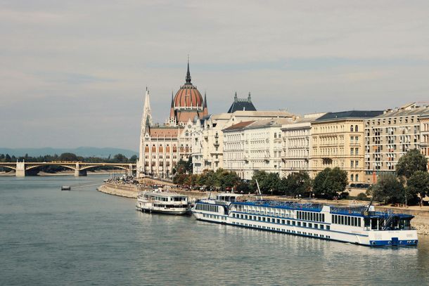Danube riverfront with historic buildings and a blue-and-white cruise boat in Budapest