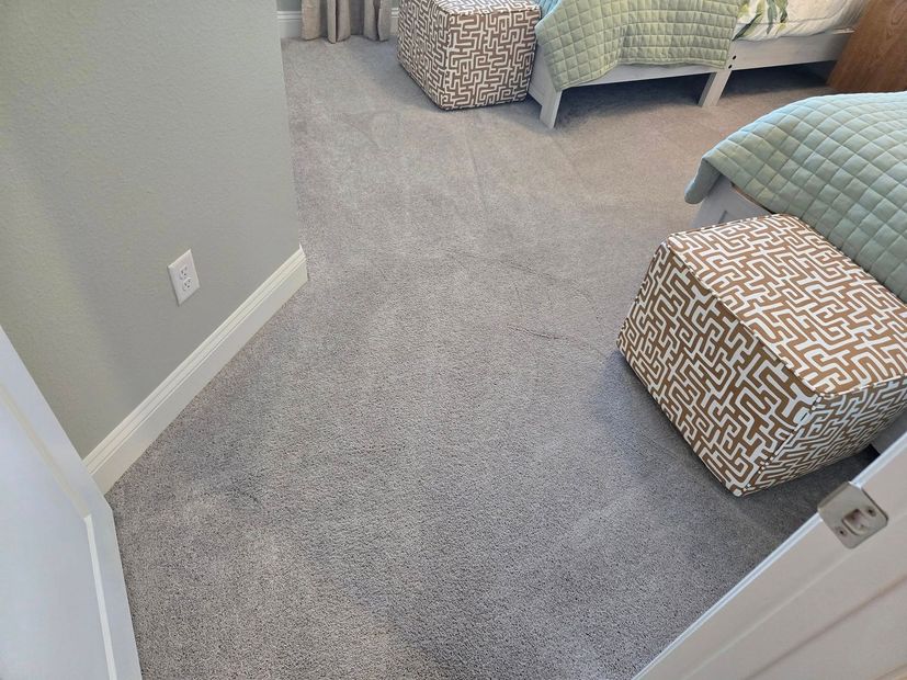 Bedroom interior with grey carpet, white baseboards, and two patterned cube ottomans beside beds with light green quilts.