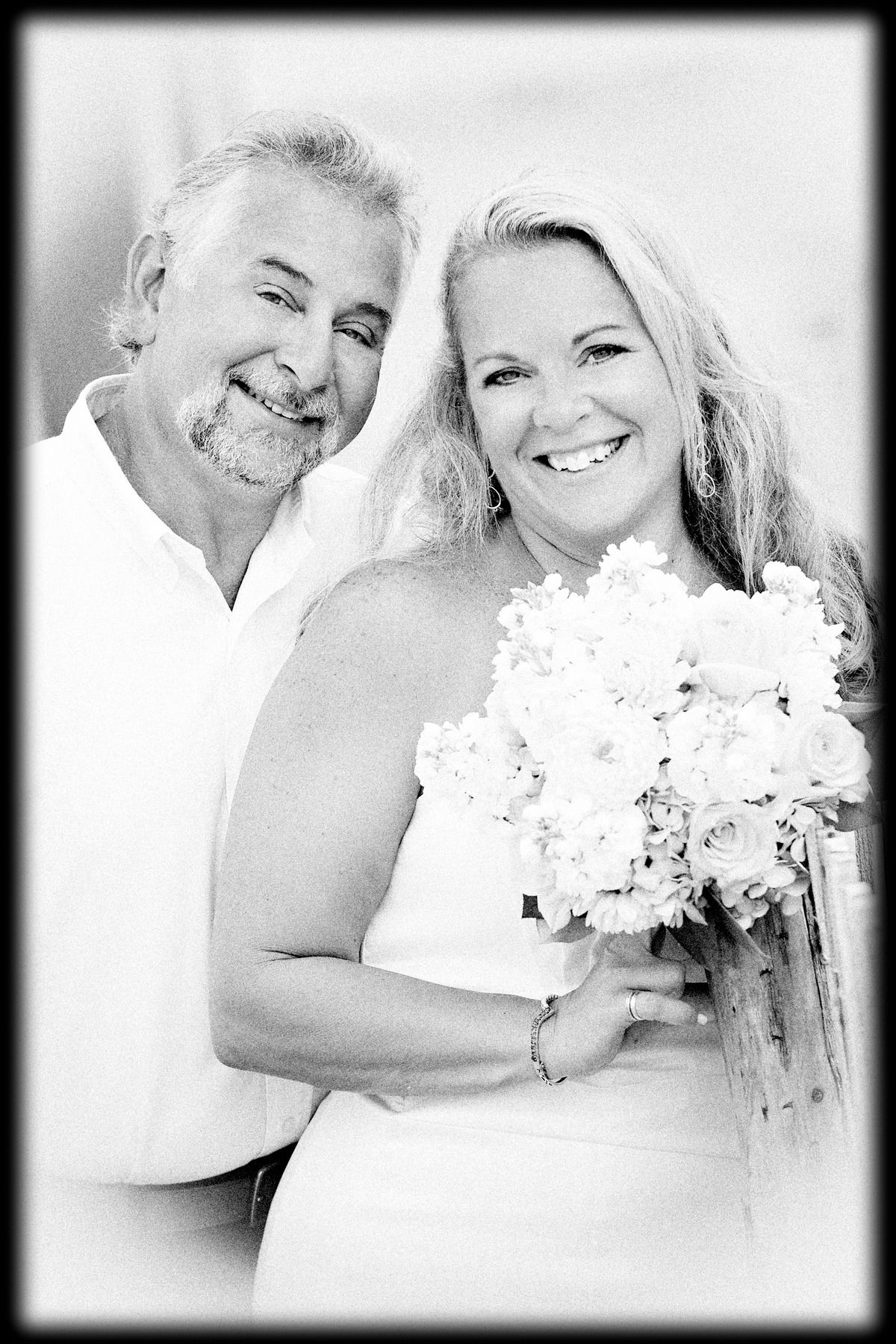 A man and a woman are posing for a black and white photo . the woman is holding a bouquet of flowers.