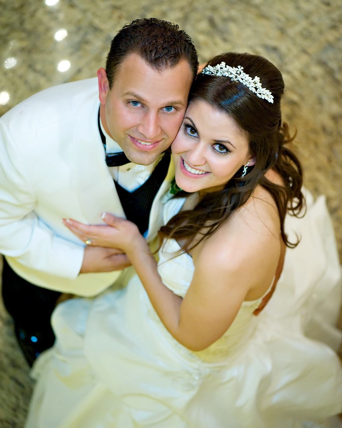 A bride and groom are posing for a picture and the bride is wearing a tiara