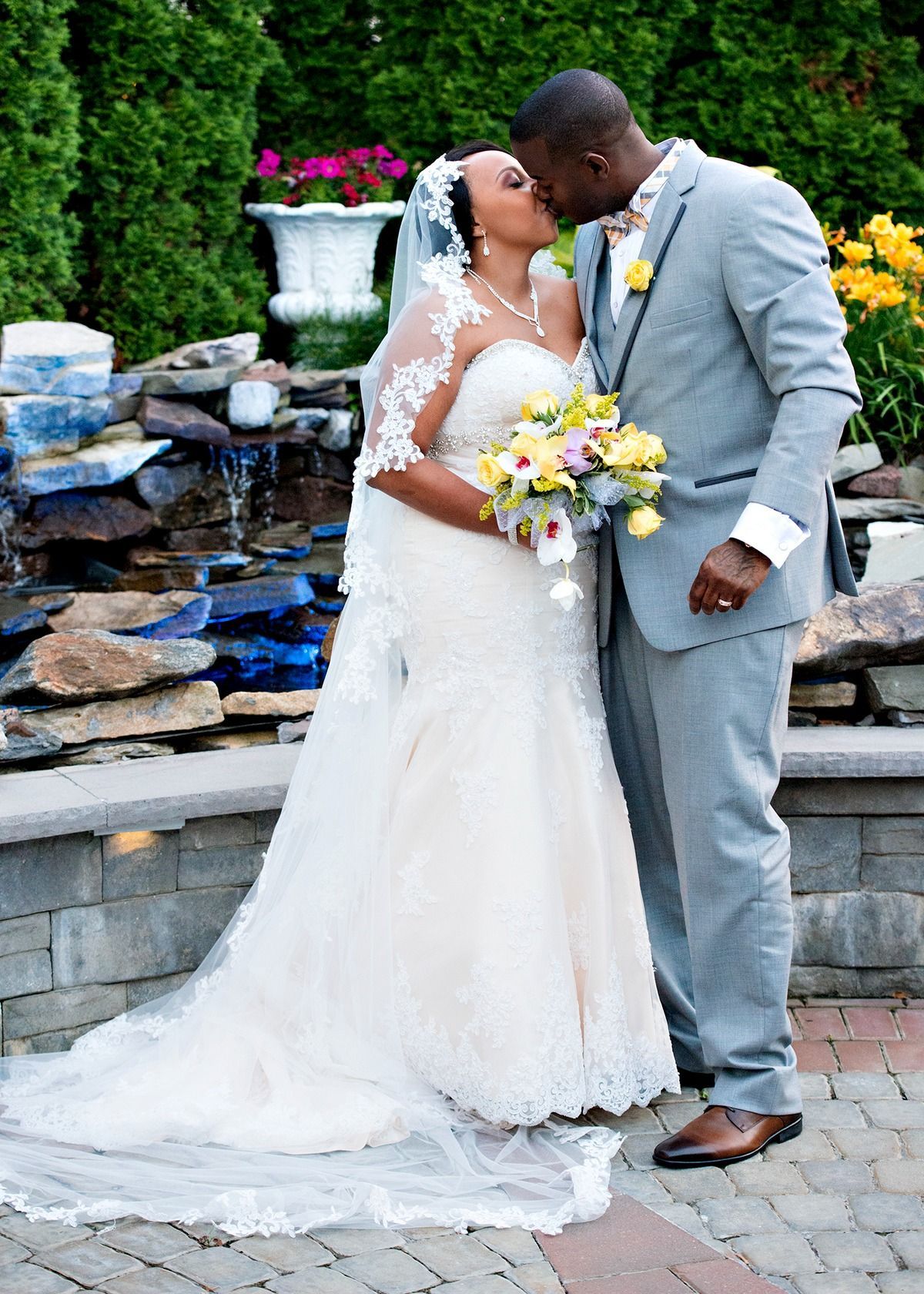 A bride and groom are kissing in front of a waterfall.